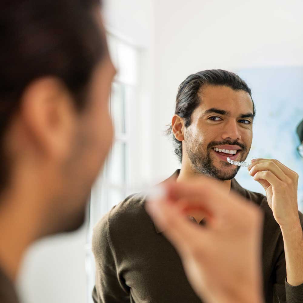 Man holding an Invisalign aligner looking in a mirror